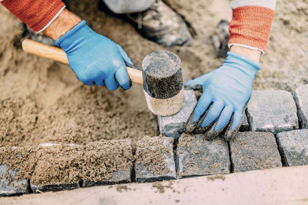 Construction worker placing stone tiles, cobblestone blocks in s